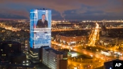 FILE - An electronic screen, installed on the facade of a business tower, shows an image of Russian President Vladimir Putin speaking during his annual state of the nation address, in St. Petersburg, Russia, April 21, 2021.