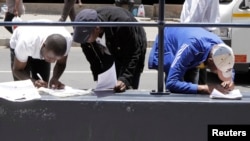 FILE - Zimbabweans fill out application forms outside Immigration offices in Johannesburg.