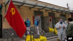Para pekerja masyarakat berbincang di luar sebuah lingkungan di Beijing, China yang sedang menjalani karantina wilayah untuk menahan penyebaran COVID-19, Kamis, 17 Maret 2022 (Foto: Ng Han Guan/AP Photo)