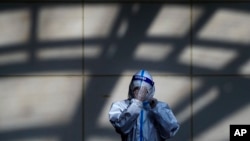 A worker in protective suit wipes his face shield at a coronavirus testing side in Beijing, Monday, Dec. 5, 2022. 