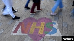FILE - Shoppers walk past artwork denoting appreciation for the U.K. National Health Service, on Oxford Street in London, Oct. 20, 2021