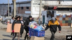 FILE - Local residents carry water from the food warehouse, on the territory which is under the Government of the Donetsk People's Republic control, on the outskirts of Mariupol, Ukraine, March 18, 2022. 