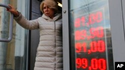 FILE - In this Feb. 24, 2022, photo, a woman leaves an exchange office, where a screen showing the currency exchange rates of the U.S. dollar and euro to Russian rubles is displayed, in Moscow.