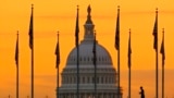 An early morning pedestrian is silhouetted against sunrise as he walks through the US flags on the National Mall and past the US Capitol Building in Washington, Nov. 7, 2022.