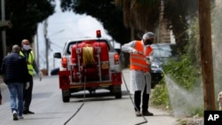 FILE - A Palestinian worker sprays disinfectant as a preventive measure to help contain the coronavirus, in the West Bank city of Nablus, April 8, 2020. 