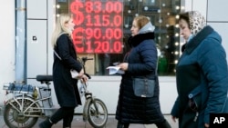 FILE - People walk past a currency exchange office screen displaying the exchange rates for the U.S. dollar and the euro to Russian rubles in Moscow, Feb. 28, 2022.