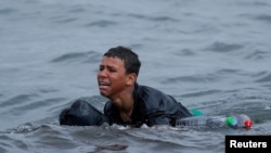 FILE - Achraf, 16, cries as he swims using bottles as floaters, near the fence between the Spanish-Moroccan border, after thousands of migrants swam across the border, in Ceuta, Spain, May 19, 2021. 