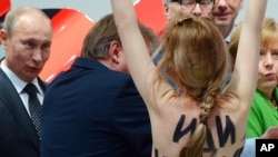 A topless demonstrator with written messages on her back walks towards Russian President Vladimir Putin (L) and German Chancellor Angela Merkel (R) during the opening tour at the Hannover Fair, Hannover, Germany, April 8, 2013. 