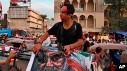 FILE - Protester hits a poster showing the leader of the Iranian Revolutionary Guard's foreign wing, or Quds Force, Gen. Qassim Soleimani with a shoe during ongoing anti-government protests in Baghdad, Nov. 3, 2019.