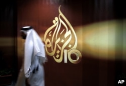 FILE - A Qatari employee of the Al Jazeera Arabic-language TV news channel walks past the logo of Al Jazeera in Doha, Qatar.