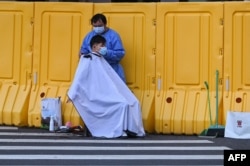 A man gets a haircut on a street next to a locked down neighborhood during a COVID-19 lockdown in the Jing'an district of Shanghai, May 30, 2022.