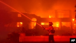 A firefighter works to put out a building burning during a wildfire May 11, 2022, in Laguna Niguel, Calif. 