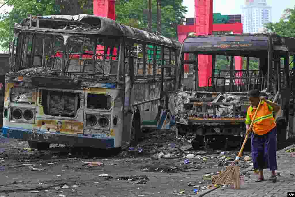 A worker sweeps the street alongside the burnt buses near Sri Lanka's former prime minister Mahinda Rajapaksa's official residence, a day protests in Colombo, Sri Lanka.
