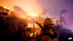 A firefighter works to put at a burning building during a wildfire May 11, 2022, in Laguna Niguel, Calif.