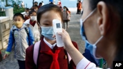 FILE - A teacher takes the body temperature of a schoolgirl to help curb the spread of the coronavirus before entering Kim Song Ju Primary School in Central District in Pyongyang, North Korea, Oct. 13, 2021.