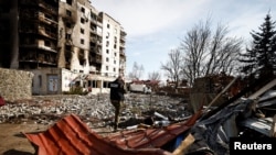 Anggota tim jaksa kejahatan perang berbicara melalui telepon di samping bangunan yang dihancurkan Rusia, di Borodyanka, wilayah Kyiv, Ukraina 7 April 2022. (Foto: REUTERS/Zohra Bensemra)
