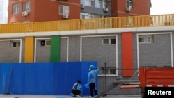Workers wearing personal protective equipment (PPE), install a barricade around a residential area under lockdown while a resident looks out from a window, amid the coronavirus disease (COVID-19) outbreak in Beijing, China, May 4, 2022.