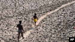 FILE - A man and a boy walk across the drying bed of river Yamuna in India, May 2, 2022. According to a report released by the World Meteorological Organization on May 9, 2022, the world is creeping closer to the warming threshold international agreements are trying to prevent.