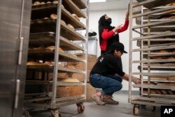 Madina Safi, 28, top, trains Marjan Enayt, 18, who is also a recent refugee from Afghanistan, as they work in a grocery store bakery in Virginia, April 14, 2022.