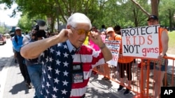 A member of the National Rifle Association plugs his ears with his fingers as he walks past protesters during the NRA's annual meeting at the George R. Brown Convention Center in Houston, May 27, 2022.