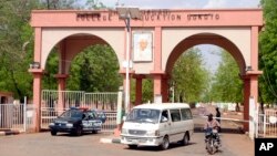 A man rides a motorbike taxi past police vehicles at the entrance of Shehu Shagari College of Education in Sokoto, Nigeria, May 13, 2022. 