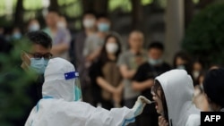 FILE - A health worker gets a swab sample from a woman to be tested for COVID-19 at a swab collection site in Beijing, May 27, 2022.
