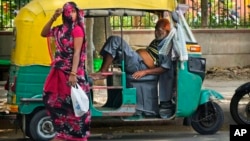An elderly auto rickshaw driver exhausted from intense heat rests in his vehicle as a woman covering her face walks past, in New Delhi, India, May 19, 2022. In spite of sporadic rains the Indian capital is still facing extreme heat conditions.