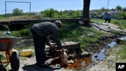 A man fills cans with water as a boy swings on on a rope in Kramatorsk, Ukraine, May 7, 2022.