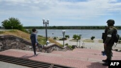 এই ছবিটি ইউক্রেনে চলমান রুশ আক্রমণের মধ্যে তোলা। খেরসন নদীর তীরে একটি ছেলে ফুটবল খেলছে, পাশে একজন রুশ সৈন্য টহল দিচ্ছে।