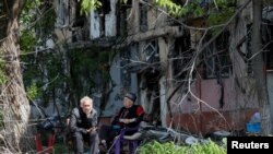 Local residents sit in a courtyard near a block of flats heavily damaged during the Ukraine-Russia conflict, in the southern port city of Mariupol, Ukraine, May 20, 2022. 