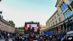 FILE - Spectators attend an award ceremony in Berlin, Germany, where a photo of Mohammad Rasoulof of Iran appears on the big screen, June 1, 2021.