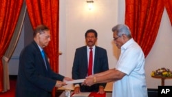 In this handout photograph provided by the Sri Lankan President's Office, President Gotabaya Rajapaksa, right, hands over the appointment document to Gamini Lakshman Peiris after he took oath of office as the new foreign minister in Colombo, Sri Lanka, Ma