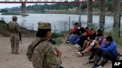 Migrantes que cruzaron el río Bravo hacia EEUU están bajo la custodia de miembros de la Guardia Nacional mientras esperan la llegada de los agentes de la Patrulla Fronteriza EEUU en Eagle Pass, Texas, el viernes 20 de mayo de 2022.