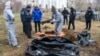 FILE - French forensics investigators, who arrived to Ukraine to investigate war crimes amid Russia's invasion, stand next to a mass grave in the town of Bucha, in Kyiv region, Ukraine, April 12, 2022.
