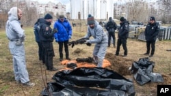 FILE - French forensics investigators, who arrived to Ukraine to investigate war crimes amid Russia's invasion, stand next to a mass grave in the town of Bucha, in Kyiv region, Ukraine, Apr. 12, 2022.