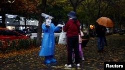 A worker in a protective suit guides people to scan health QR code at a nucleic acid test booth for the coronavirus disease (COVID-19), in Beijing, China, Nov. 11, 2022. 