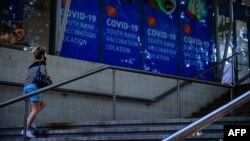 FILE - A woman walks past signage at a COVID-19 vaccination site in Brisbane, Queensland, Australia, Aug. 17, 2021.