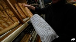 Bakery owner Florence Poirier puts baguettes in to a bag that reads, " the real taste of bread," for a customer at a bakery, in Versailles, west of Paris, Nov. 29, 2022.
