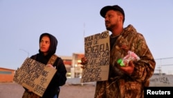 Julio Marquez and Yalimar Chirinos, migrants from Venezuela, display signs near the border between the United States and Mexico, in Ciudad Juarez, Mexico, Jan. 7, 2023. The signs reads "Hello friends, we are from Venezuela, support us with what comes out from your heart."