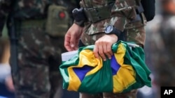 A soldier collects national flags after supporters of former Brazilian former President Jair Bolsonaro left the encampment set up outside army headquarters in Brasilia, Brazil, Jan. 9, 2023.