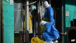 Workers in protective gear prepare to collect COVID samples from a woman at her locked down store in Beijing, Dec. 1, 2022. 