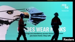 FILE - Essential workers walk past a 'Heroes Wear Masks' sign on the first day of a seven-day lockdown as the state of Victoria looks to curb the spread of a coronavirus disease (COVID-19) outbreak in Melbourne, Australia, May 28, 2021. 
