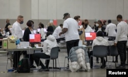 Petugas pemilu Detroit memasukkan surat suara yang tidak hadir ke mesin tabulasi selama pemilihan paruh waktu di Huntington Place di Detroit, Michigan, AS 8 November 2022. (Foto: REUTERS/Rebecca Cook)