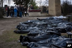 A family mourns a relative killed during the war with Russia, as dozens of black bags containing more bodies of victims are seen strewn across the graveyard in the cemetery in Bucha, in the outskirts of Kyiv, Ukraine, April 11, 2022.