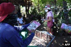 Seorang sukarelawan (kanan) untuk calon presiden oposisi dan wakil presiden saat ini, Leni Robredo, membagikan brosur kepada penduduk selama kampanye dari rumah ke rumah di kota Pasuquin, provinsi Ilocos Norte, 26 Maret 2022. (Foto: Ted ALJIBE / AFP)