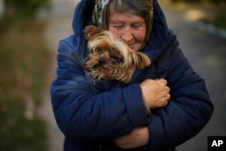 A woman warms her dog in Kivsharivka, Ukraine, Sunday, Oct. 16, 2022. As temperatures drop below freezing in eastern Ukraine, those who haven't fled from the heavy fighting, regular shelling and months of Russian occupation are now on the threshold of a brutal winter.