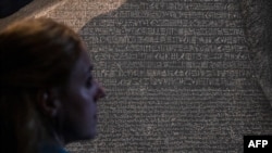 A member of the British Museum staff looks at the Rosetta Stone on Oct. 11, 2022, displayed for the exhibition "Hieroglyphs: Unlocking Ancient Egypt," which runs at the London museum Oct. 13 through Feb. 19, 2023. 