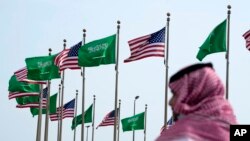 FILE - A man stands under U.S. and Saudi Arabian flags prior to a visit by President Joe Biden, at a square in Jeddah, Saudi Arabia, July 14, 2022. 