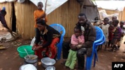 FILE - Members of a family of refugees from the Democratic Republic of Congo sit by their makeshift hut at the Kenani refugee transit camp in Nchelenge, Zambia, Oct. 30, 2017.