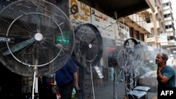 FILE - A man stands by fans spraying air mixed with water vapor deployed by donors to cool down pedestrians along a street in Iraq's capital Baghdad on June 30, 2021, amidst a severe heat wave.